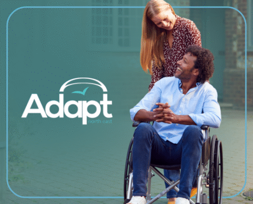 A woman pushing a man in a wheelchair, both smiling. Adapt logo.