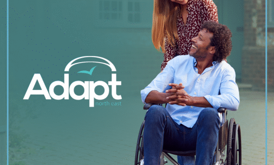 A woman pushing a man in a wheelchair, both smiling. Adapt logo.