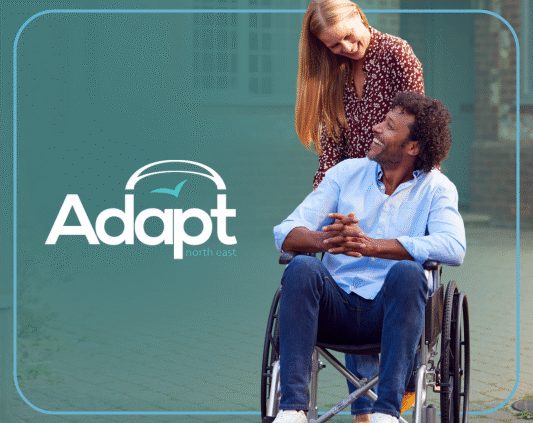 A woman pushing a man in a wheelchair, both smiling. Adapt logo.